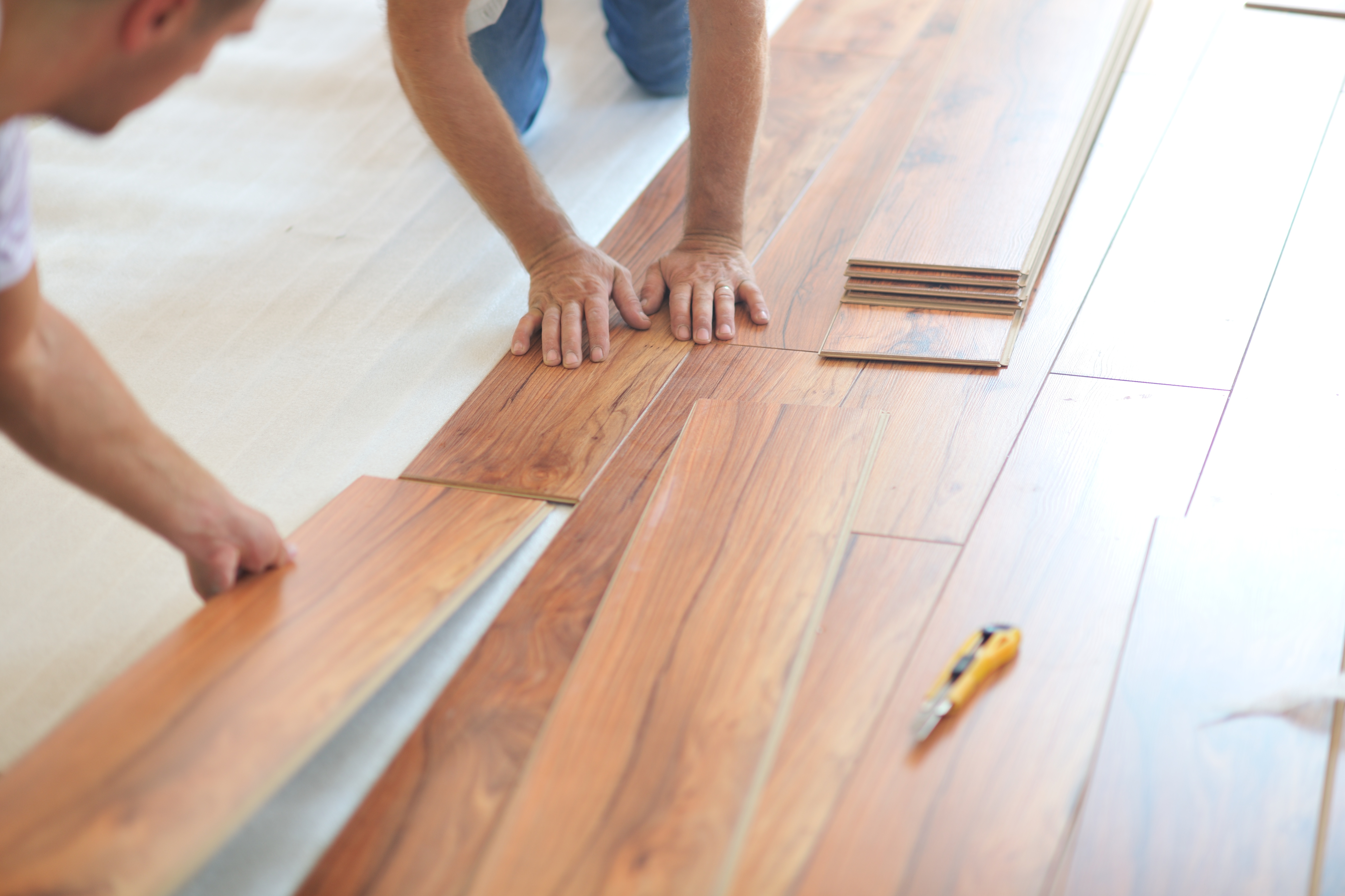 Workers installing laminate flooring planks on subfloor with tools nearby