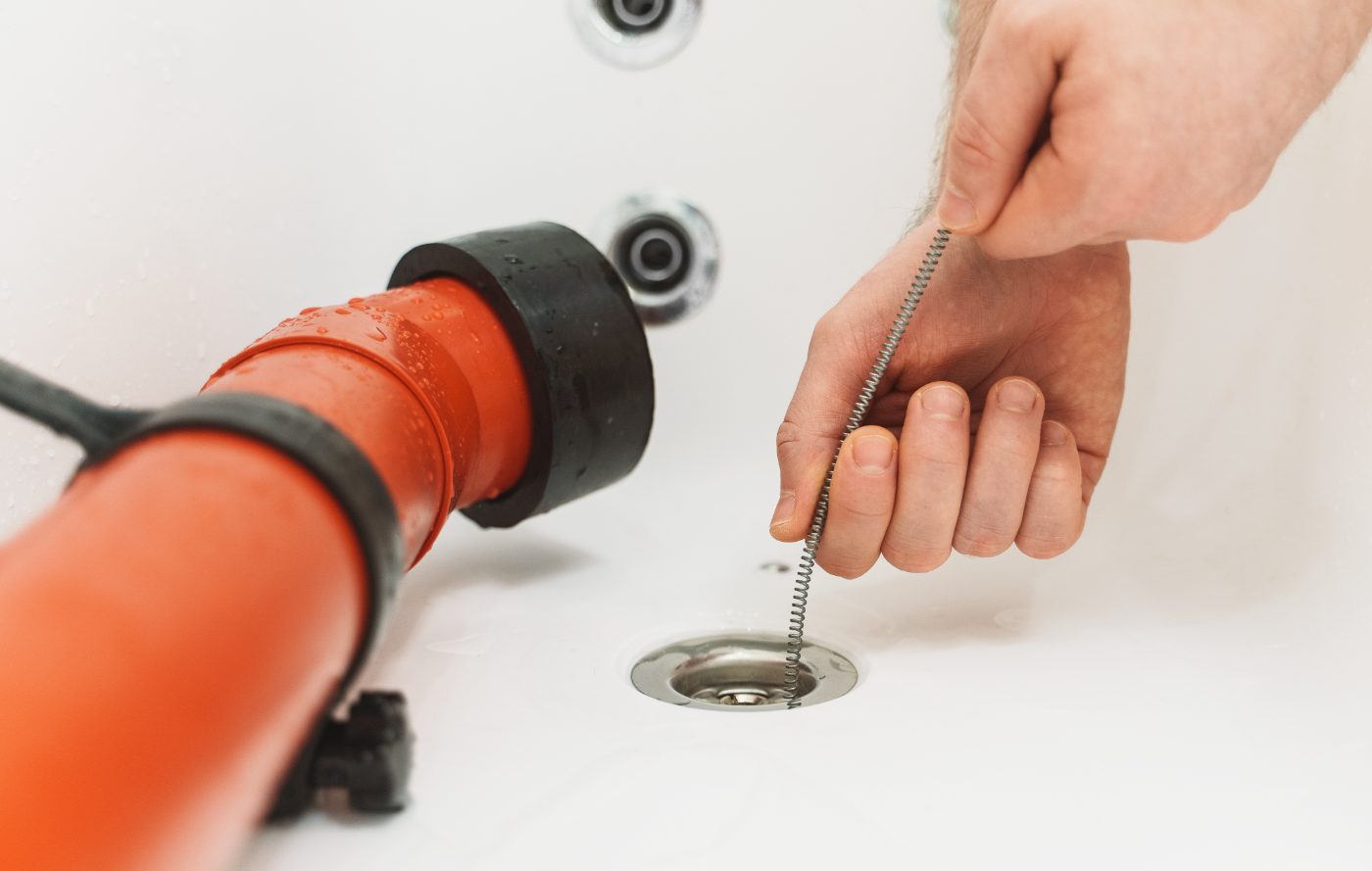 Plumber using electric drain auger cable to clear clogged drain opening in ceiling